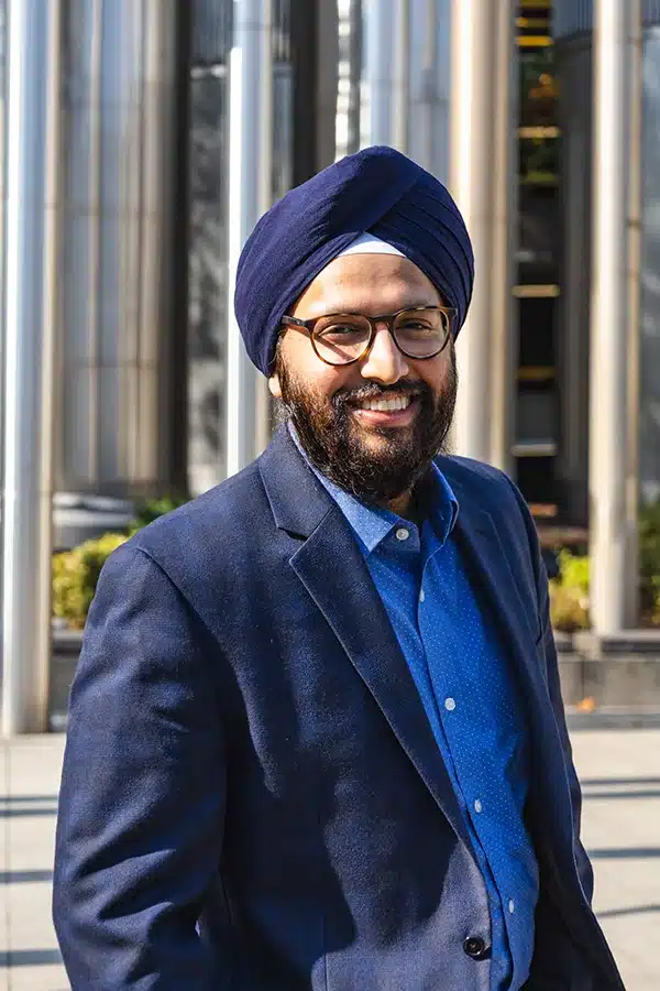 Team Portrait of Angad Singh Nirh, standing in a blue business suit and turban, in front of an industrial background.
