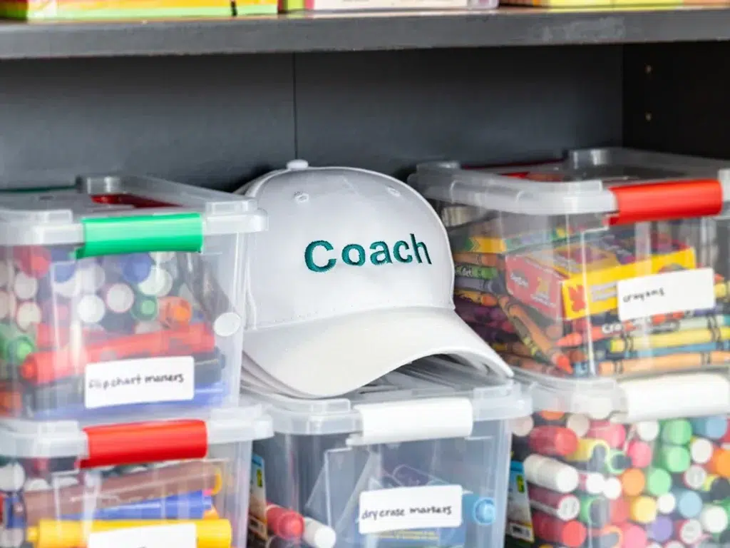 Image banner for the "about the company section", showing a baseball cap with a logo that reads "coach", amongst many workshop materials and stationary